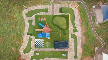 A fenced outdoor area with a playground, a small building, a pool, and a checkered game board.