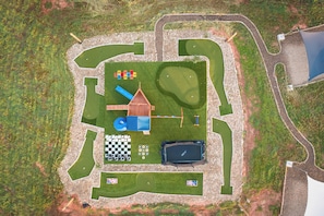 A fenced outdoor area with a playground, a small building, a pool, and a checkered game board.