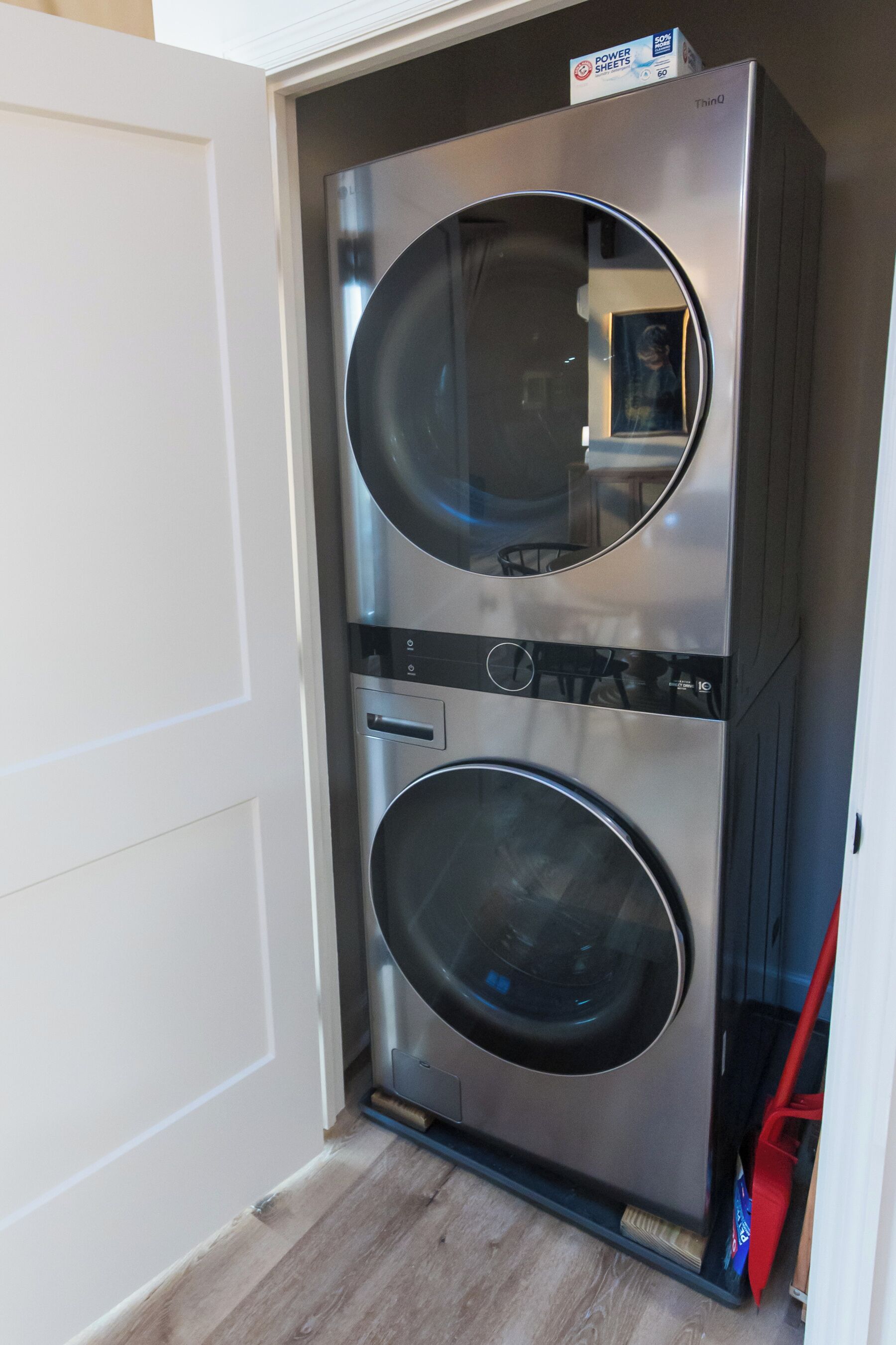 Máquina de lavar e secar roupa compacta, em aço inoxidável, instalada num espaço pequeno e fechado, com soalho de madeira.