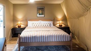 Une chambre avec un lit, deux lampes de chevet, un ventilateur de plafond, un tableau encadré au mur et une structure en forme de tente sur la droite.