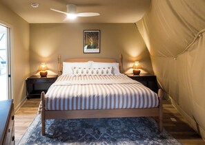 A bedroom with a bed, two bedside lamps, a ceiling fan, a framed picture on the wall, and a tent-like structure to the right. - Lake Monticello Geodome-MiniGolf-Hot Tub-Games-Playground-Stargazing-Lake Murray (Jenkinsville)