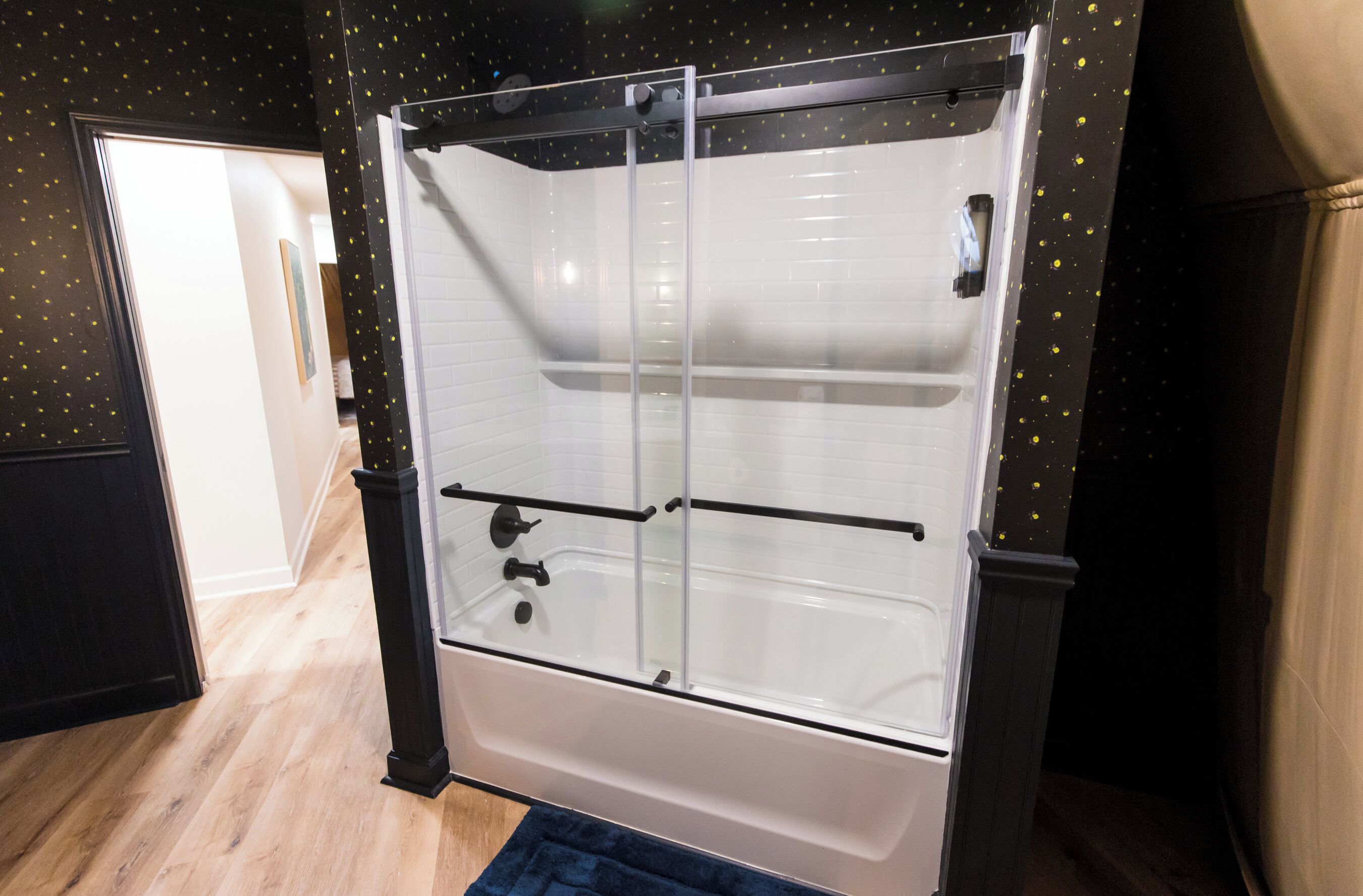 Casa de banho com cabine de chuveiro em vidro, paredes revestidas a azulejo branco e soalho em madeira.