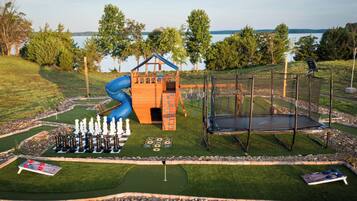 A playground with a slide, climbing wall, and trampoline, surrounded by a golf course and a lake view.