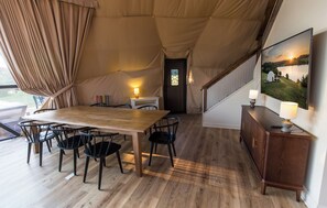 A tented accommodation with a wooden dining table, chairs, a small white cabinet, and a painting of a landscape. - Lake Monticello Geodome-MiniGolf-Hot Tub-Games-Playground-Stargazing-Lake Murray (Jenkinsville)