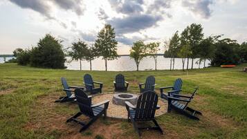 Un espace extérieur aménagé au bord du lac, avec des chaises Adirondack disposées autour d’un foyer circulaire.
