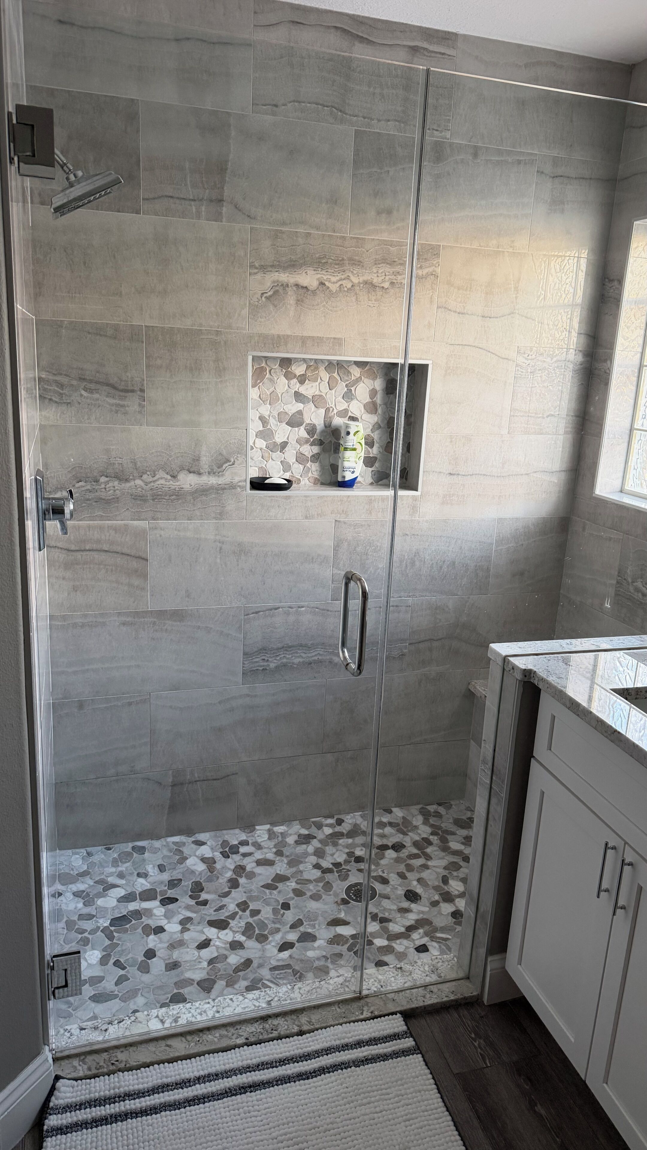 Eine Dusche mit Glastür, ein Boden mit Kieselmuster und ein Ablagebereich für Toilettenartikel.