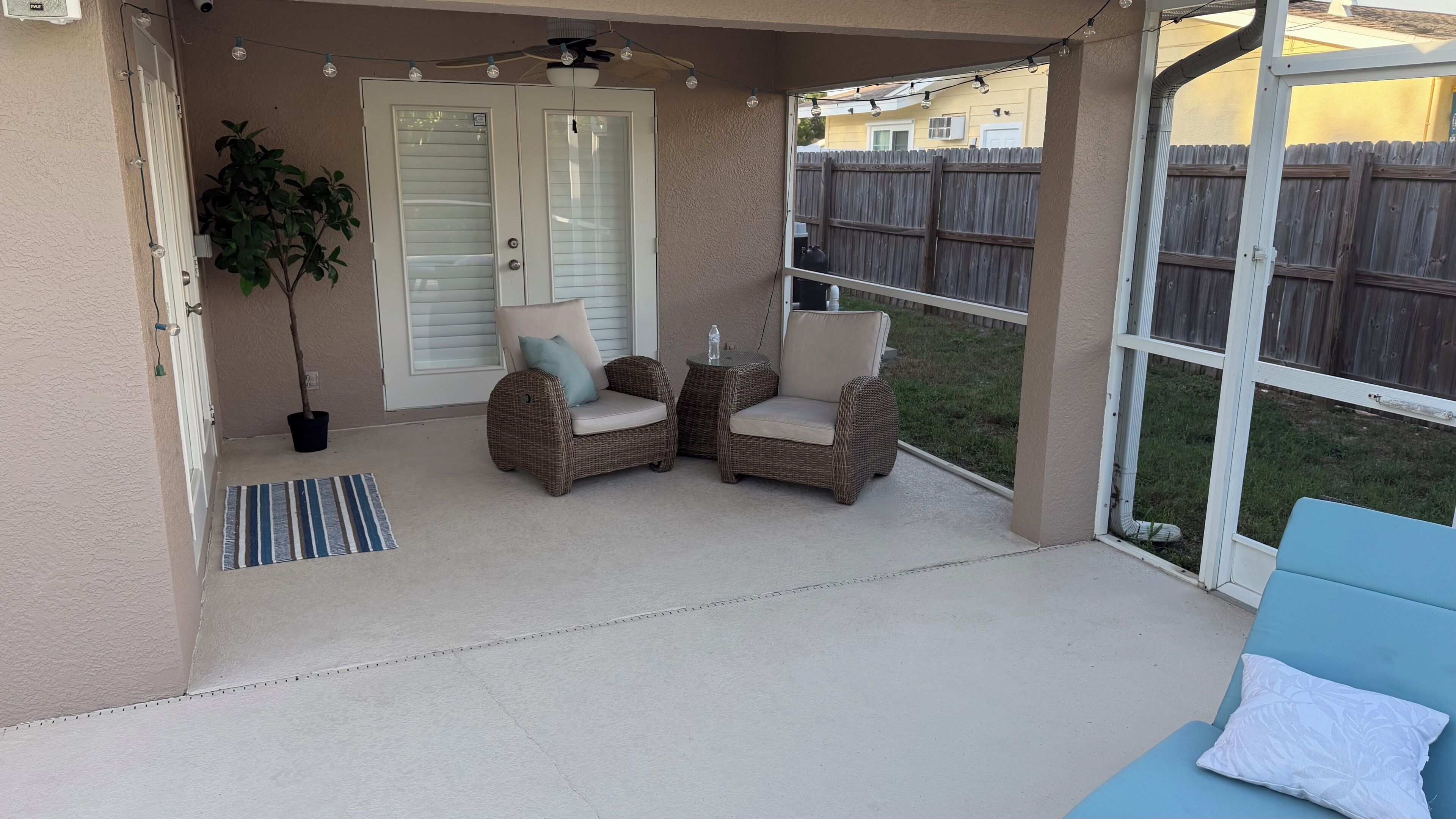 A covered patio area with two wicker chairs, a small table, and a blue lounge chair.