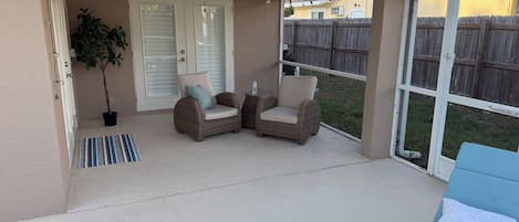 A covered patio area with two wicker chairs, a small table, and a blue lounge chair.