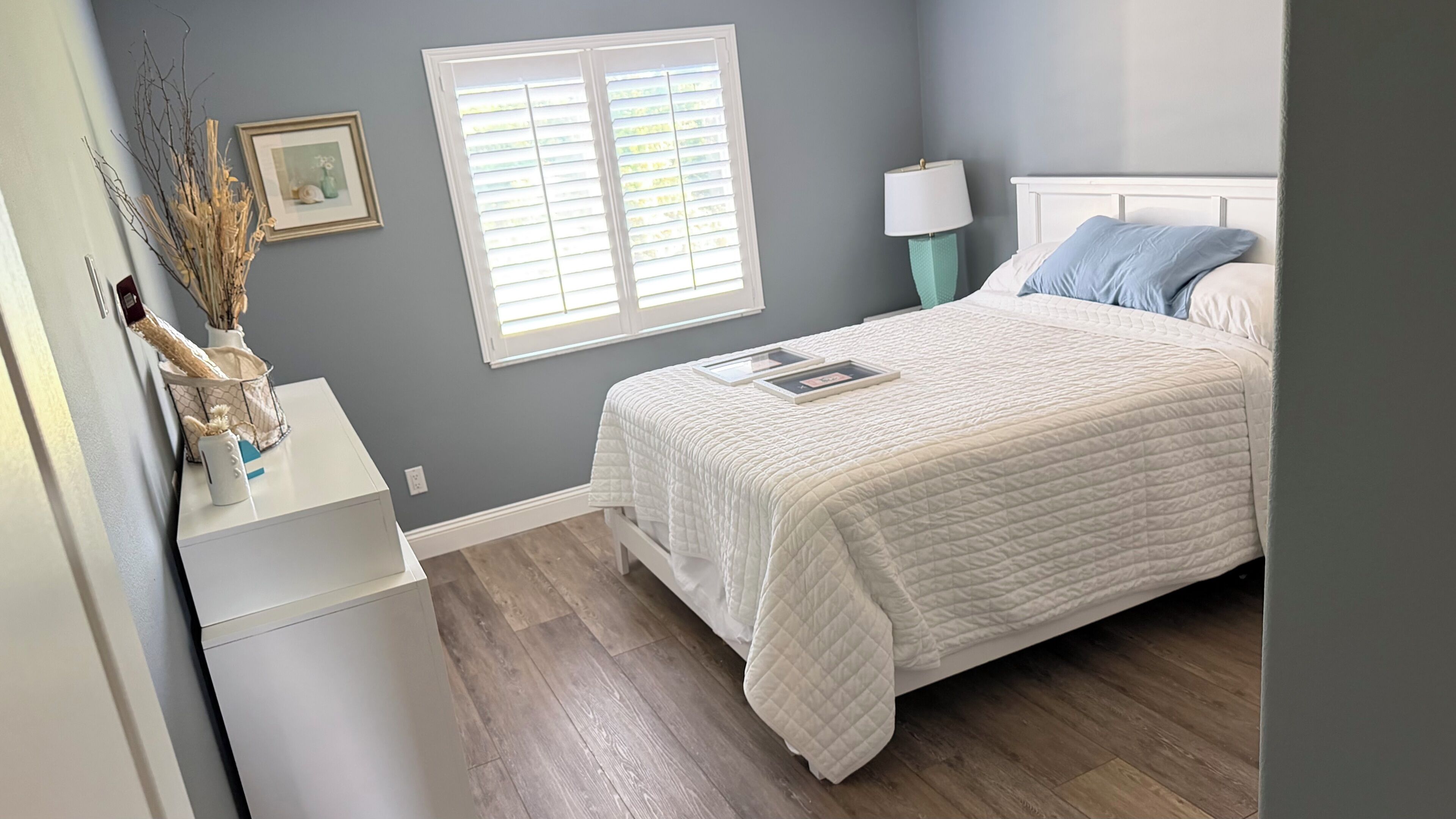 A bedroom with a bed, bedside lamp, and a window with blinds.