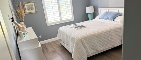 A bedroom with a bed, bedside lamp, and a window with blinds.