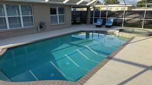 Piscina com deck revestido, área de varanda coberta com espreguiçadeiras e cerca de madeira ao fundo.