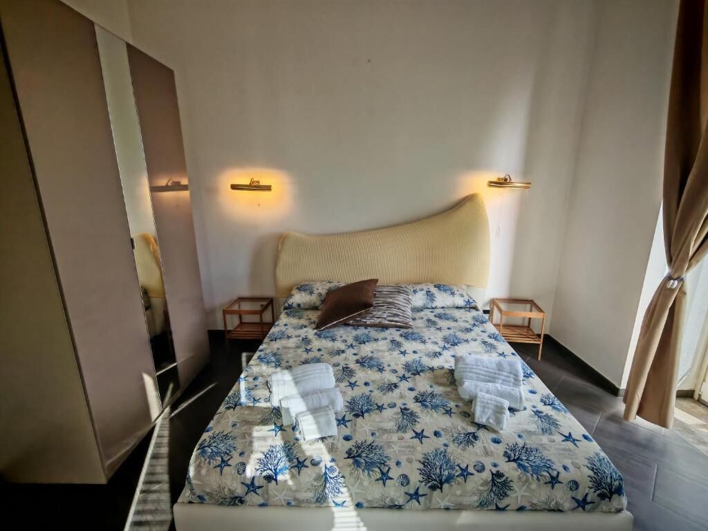 A neatly made bed with a blue and white starfish pattern, two bedside tables, and wall-mounted lights.