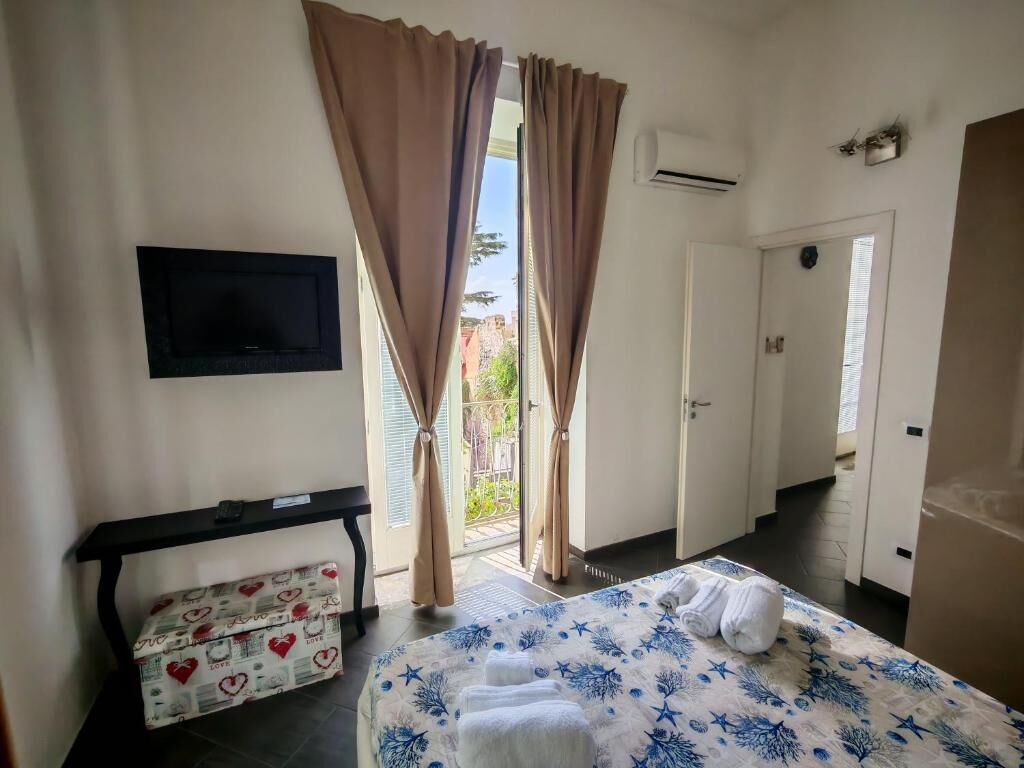 Et hotelværelse med en seng, et tv ophængt på væggen, en skydedør og et lille bord med en kasse under.
