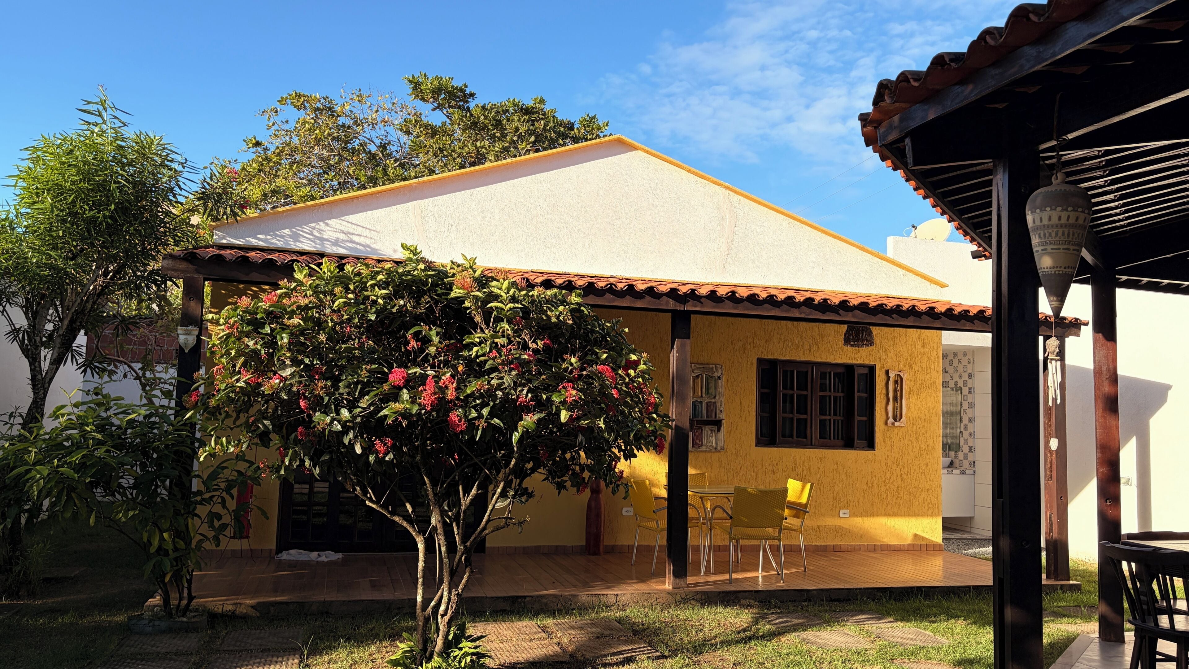 Une maison avec un toit en tuiles, un patio couvert avec des chaises et un arbre aux fleurs rouges.