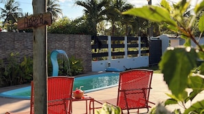 A pool area with a wooden sign, a water feature, and red chairs.
