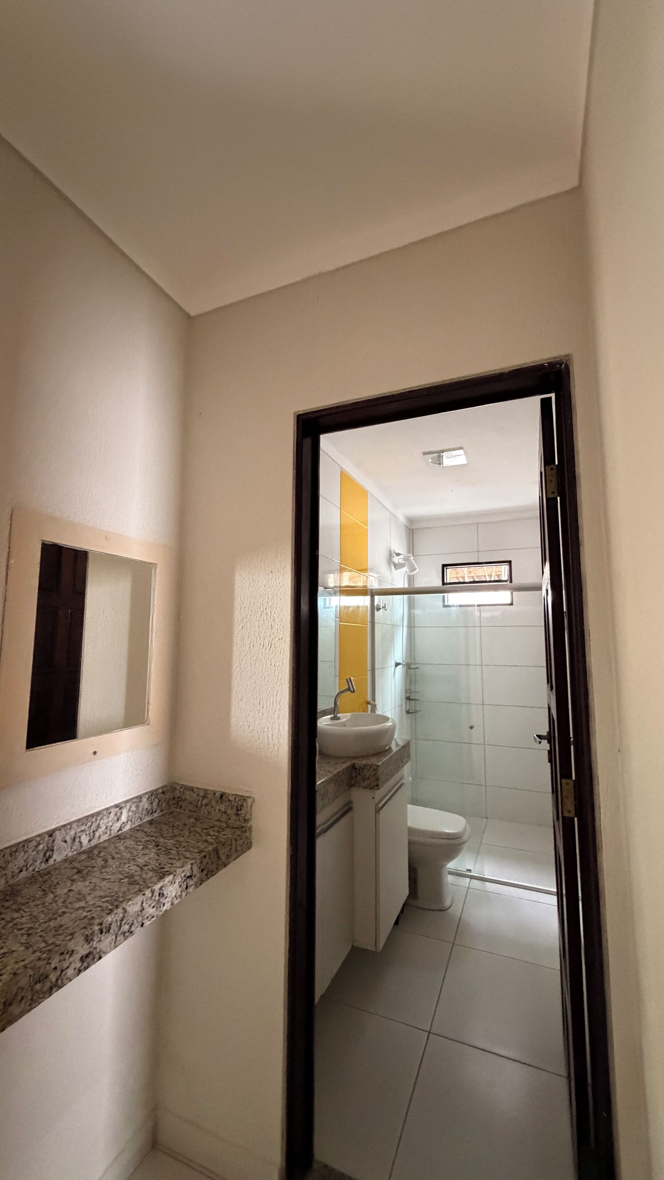Un couloir étroit mène à une salle de bain équipée d’un lavabo, de toilettes et d’une douche.