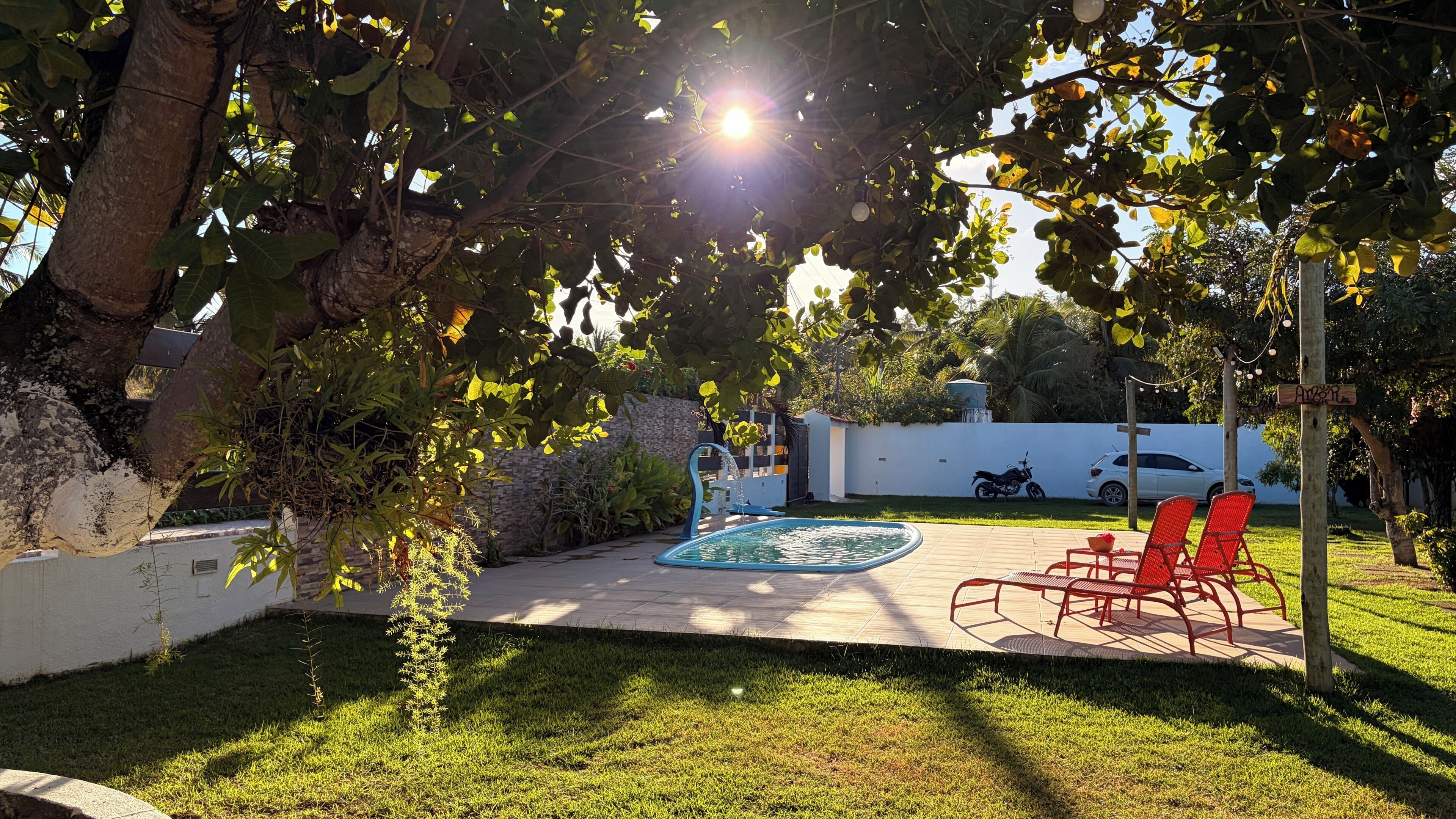 Um quintal com piscina, cadeiras vermelhas e uma fonte.