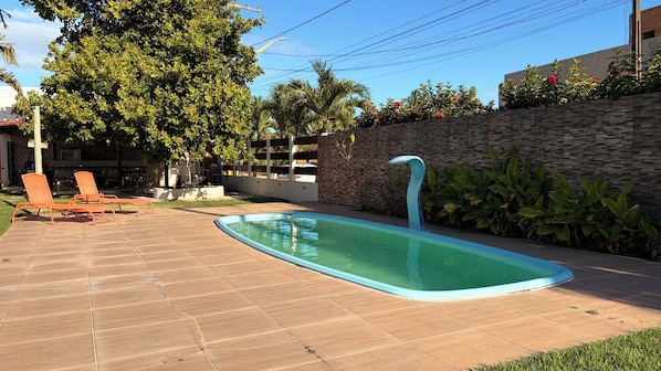 A swimming pool with a curved edge, surrounded by a stone wall and lush greenery.