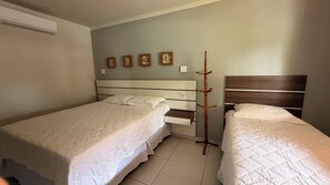 A hotel room with two beds, a wooden headboard, a wall-mounted air conditioner, and a wall with four framed pictures.