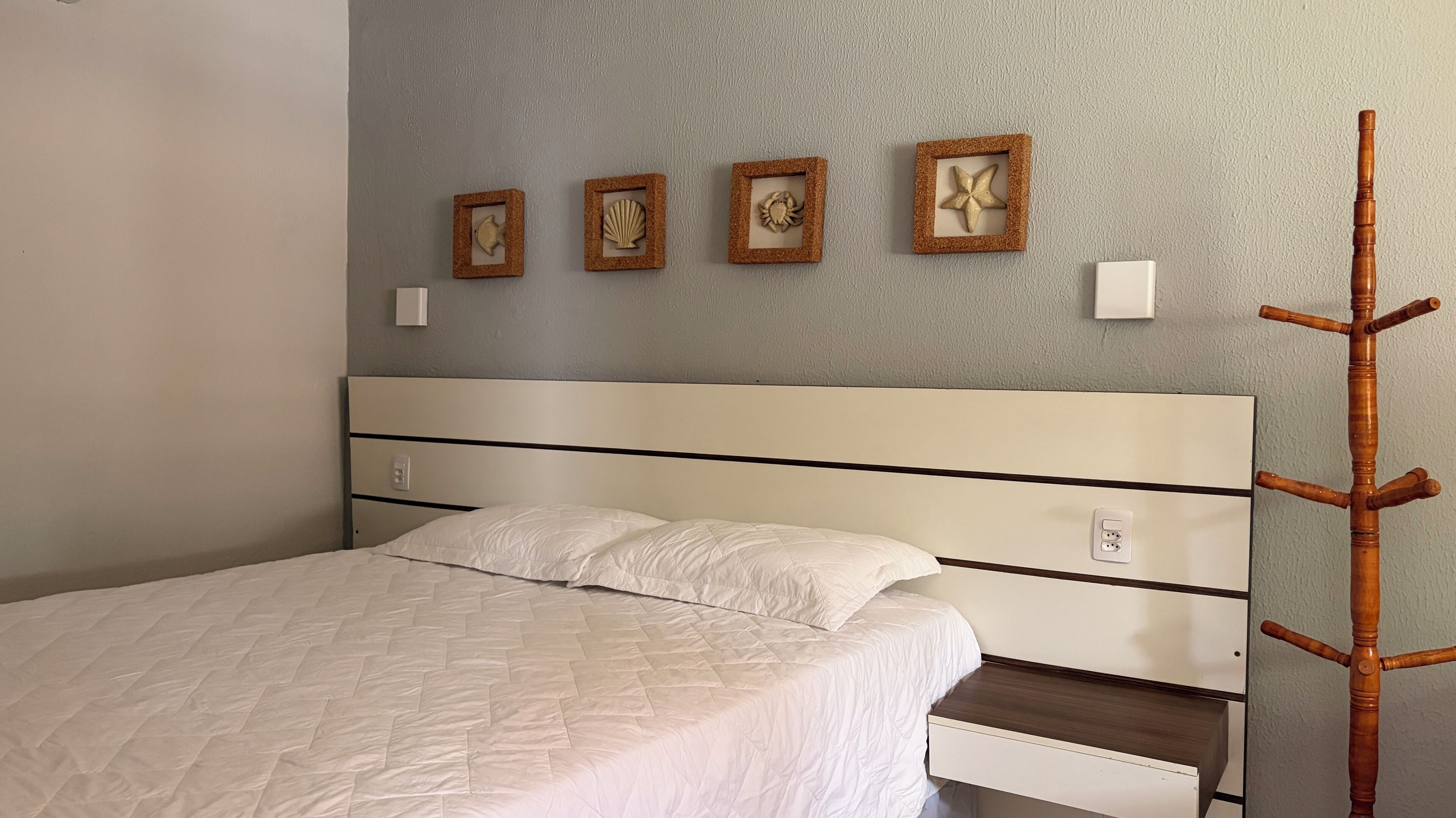 Un lit avec une couvre-lit blanche matelassée, une tête de lit en bois et une table de chevet avec un tiroir.