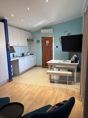 A modern kitchen with white cabinets, a dining area with a white table and bench, and a flat-screen TV mounted above the table. - 32 On Pringle (Cape Town)