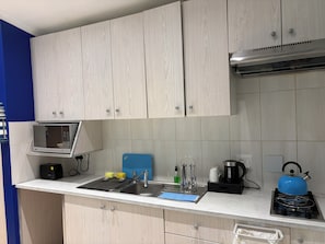 A kitchen with a microwave, toaster, sink, kettle, and a blue cutting board. - 32 On Pringle (Cape Town)