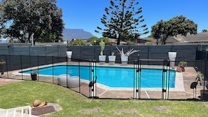 A rectangular swimming pool with a black fence, surrounded by potted plants and a grassy area. - 32 On Pringle (Cape Town)
