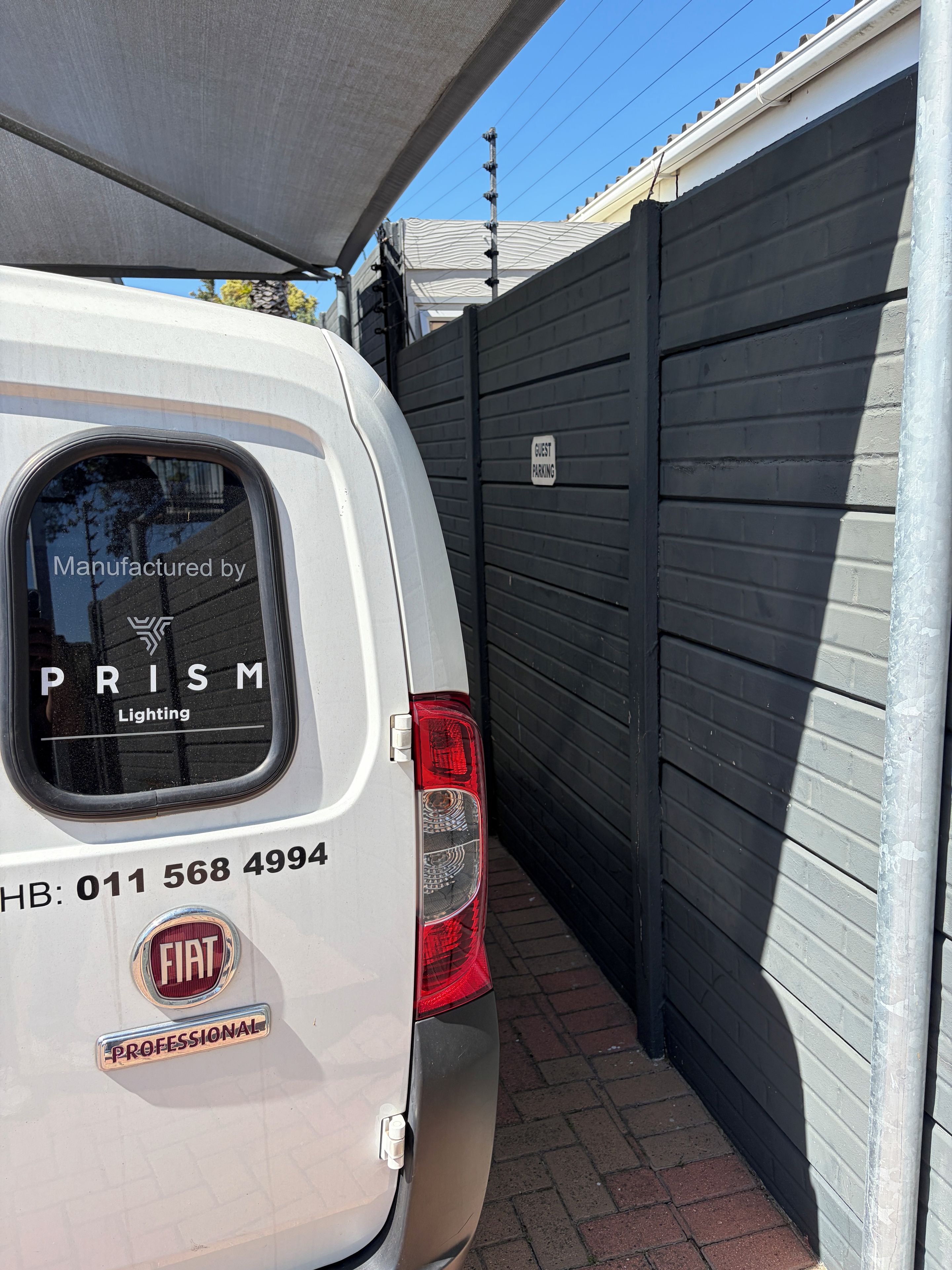Un véhicule blanc est garé à côté d’une porte de garage de couleur foncée, sur laquelle est apposée une pancarte indiquant « PARKING POUR LES VISITEURS ».