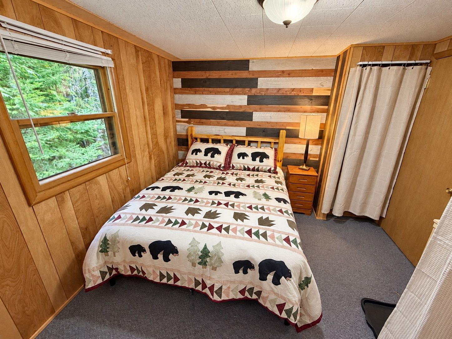A bedroom with a bed, a window, a bedside table, and a curtain.