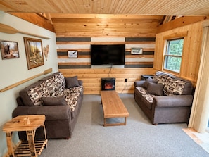 Ein gemütliches Blockhaussinnere mit Kamin, zwei Sofas, einem Fernseher und Holzwänden.