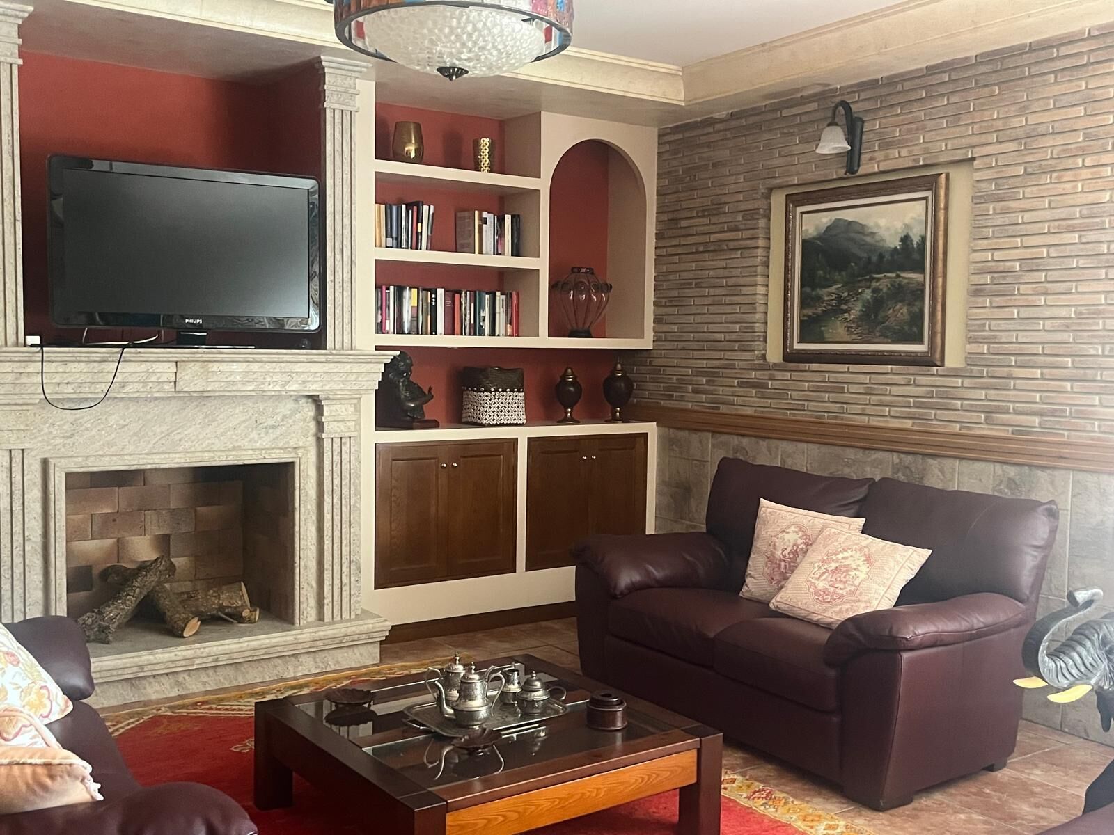 Un salon avec une cheminée, un téléviseur, une bibliothèque et un canapé en cuir marron.