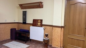 Een kamer met een houten deur, een witte radiator, een meditatiebankje, een mat en een kleine trommel.