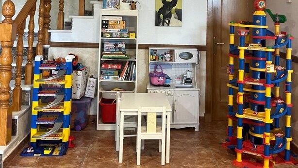 Een trap met houten spijlen, een witte muur met een lijst en een speelconstructie op de vloer.