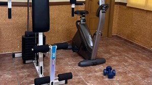 Une salle de sport équipée d’un banc de musculation, d’un appareil de cardio et d’haltères.