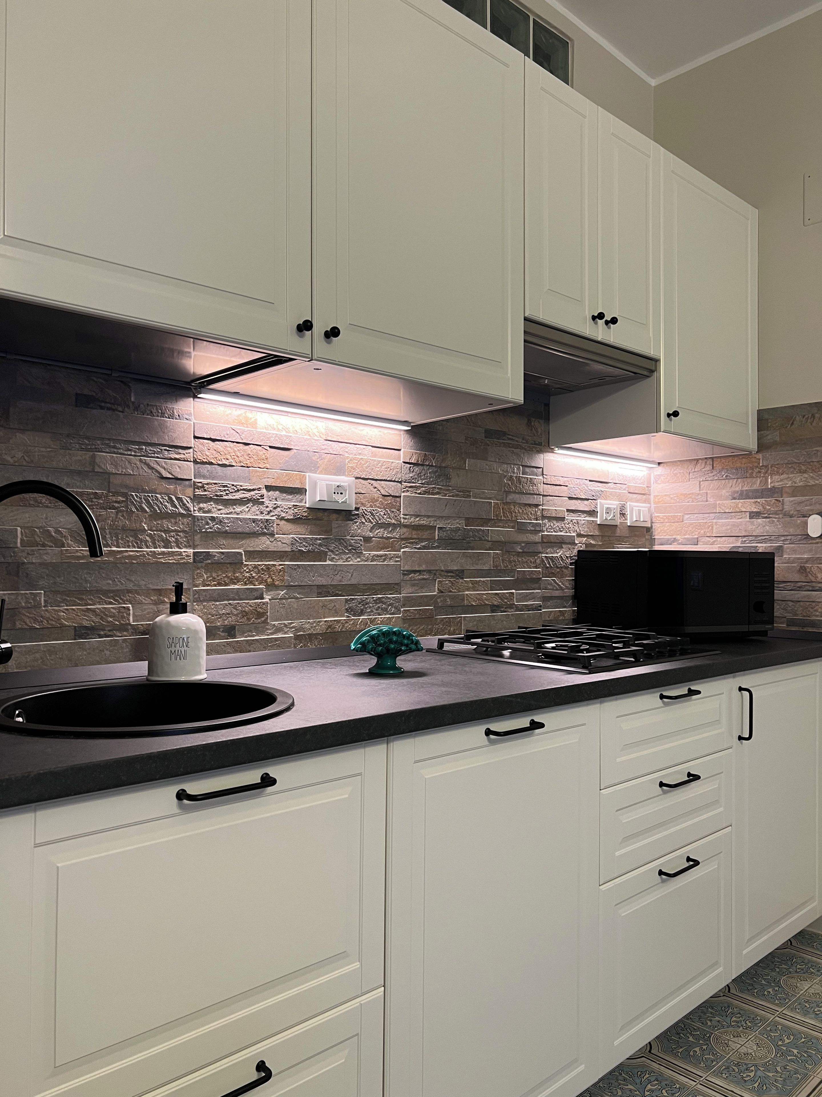A modern kitchen with white cabinets, a stone backsplash, a gas stove, and a black microwave.