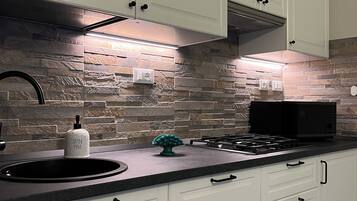 A modern kitchen with white cabinets, a stone backsplash, a gas stove, and a black microwave.