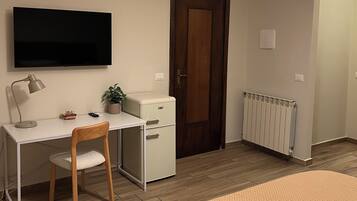 A bedroom with a bed, a desk with a chair, a television, a radiator, and a door.