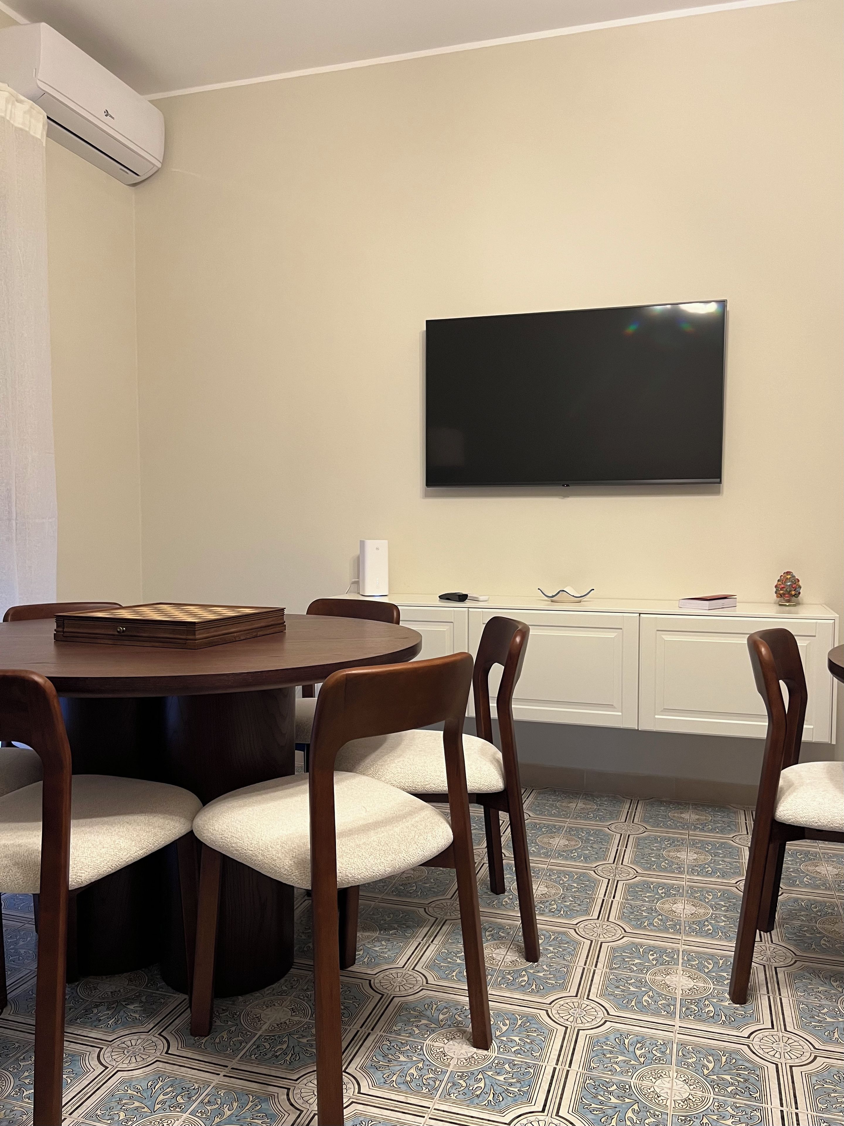 A conference room with a round table, four chairs, a flat-screen TV mounted on the wall, and a patterned floor.