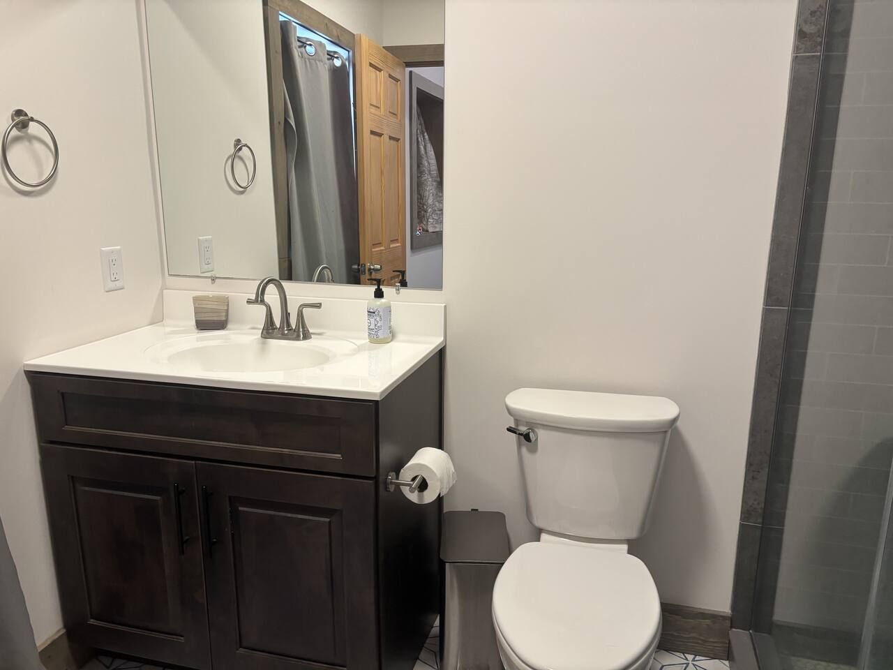 A bathroom with a white sink, dark cabinets, a toilet, and a shower area.