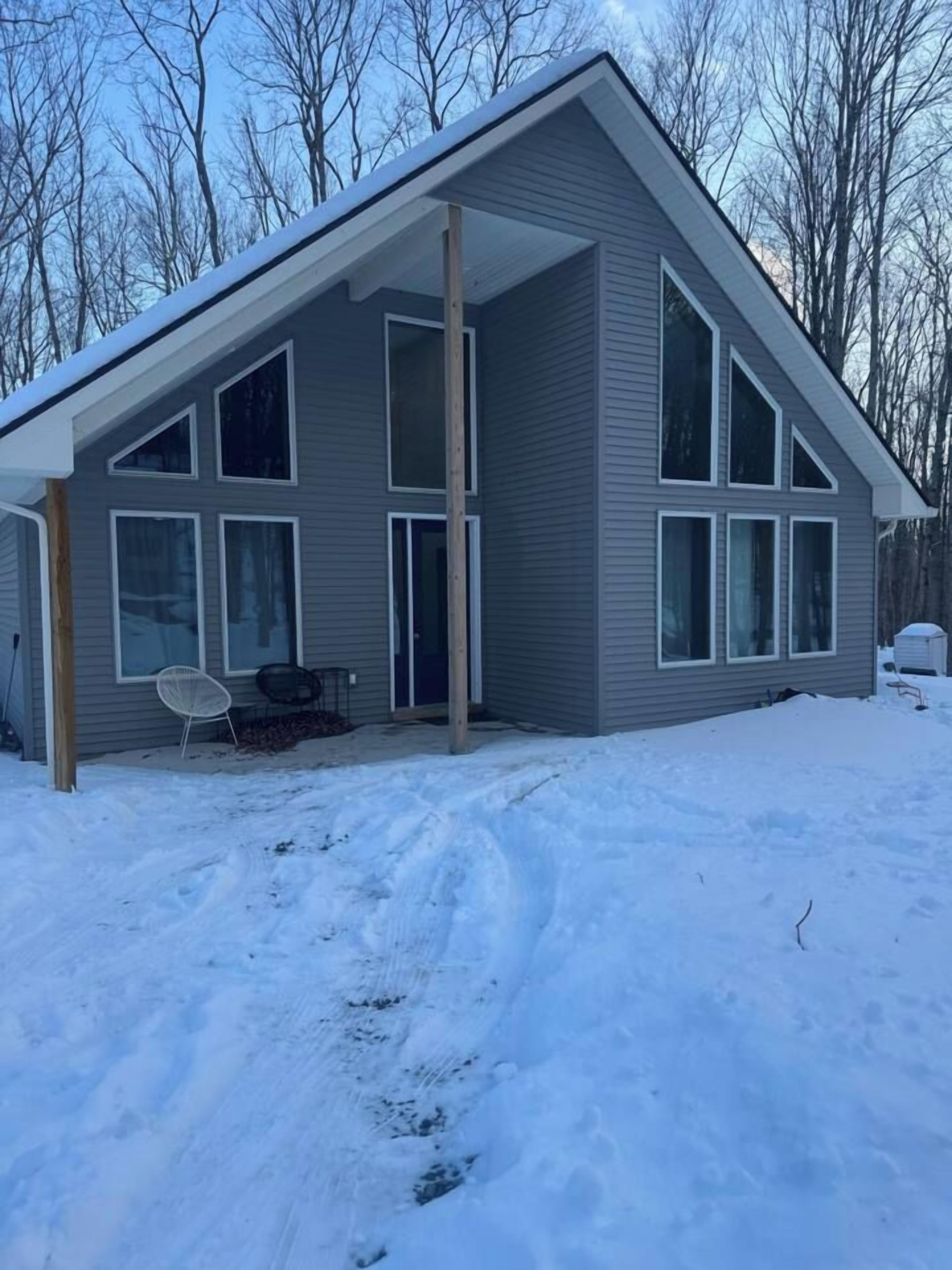 A two-story house with a covered porch, large windows, and a snow-covered yard.