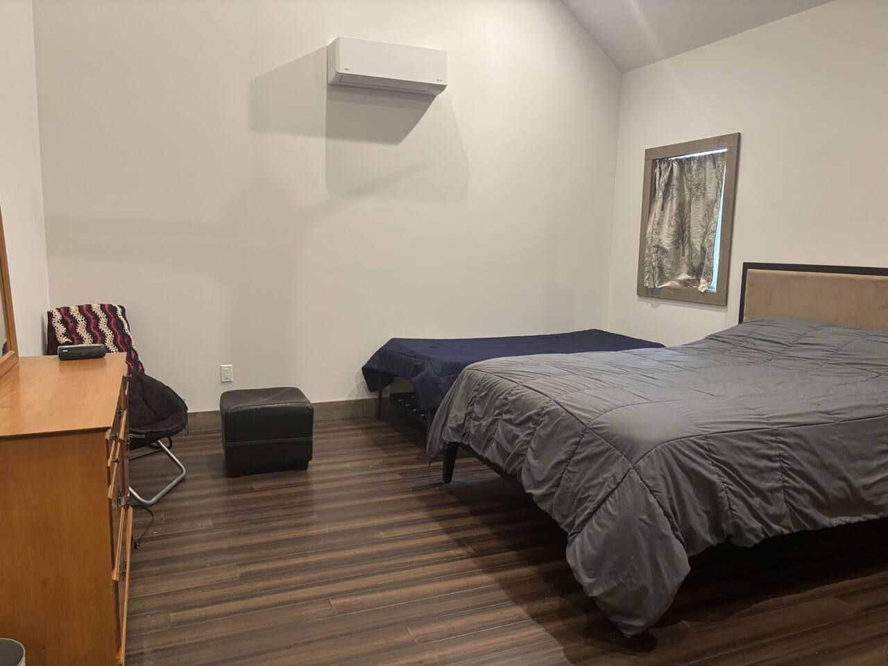Una habitación con cama, escritorio, silla, maleta y aire acondicionado instalado en la pared.