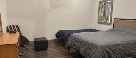 Una habitación con cama, escritorio, silla, maleta y aire acondicionado instalado en la pared.