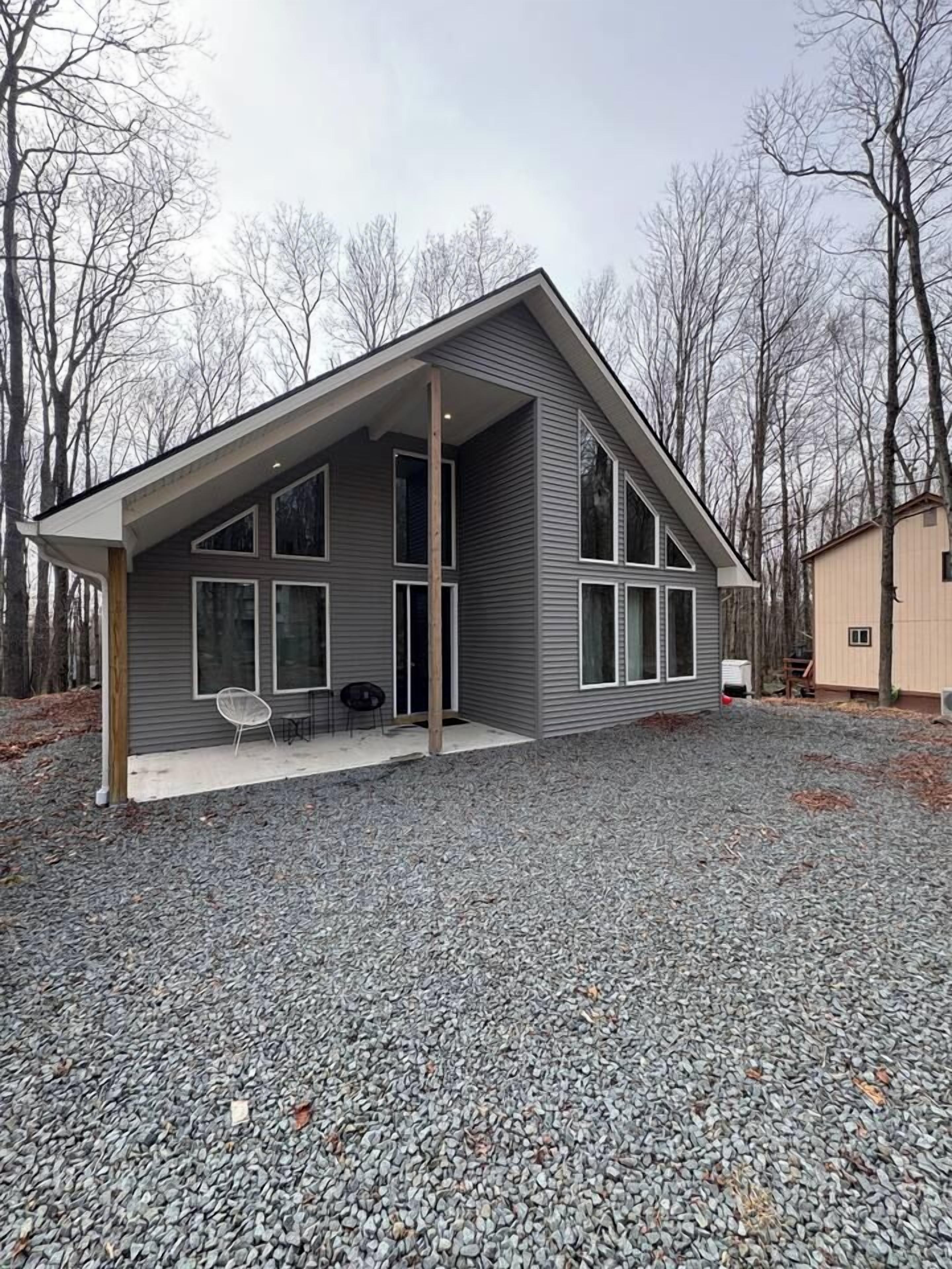 A modern house with a covered porch, large windows, and a gravel driveway.