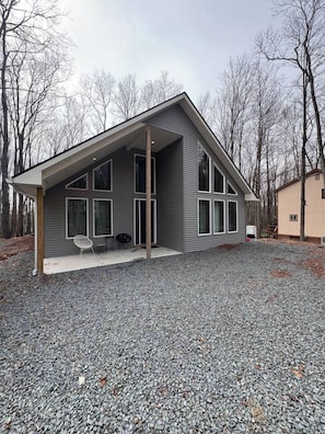A modern house with a covered porch, large windows, and a gravel driveway. - Cozy modern family build in the woods w/ hot tub! (Cobbs Lake Preserve)