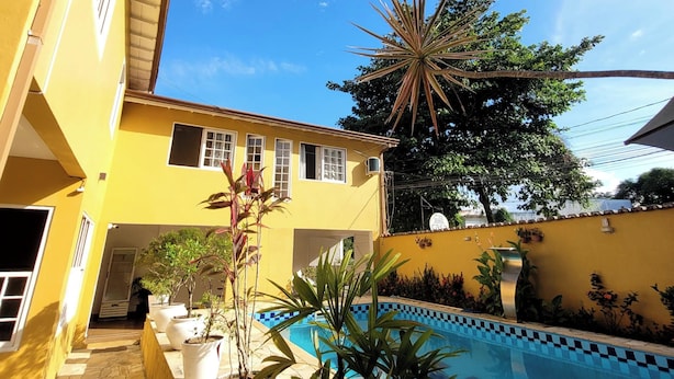 A yellow building with a swimming pool, potted plants, and a clear blue sky. - Pousada Casa Hospedaria (Paraty)
