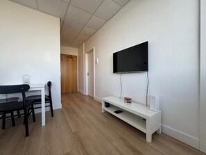 Uma sala de estar moderna com televisão de tela plana presa na parede, um móvel branco para entretenimento abaixo e uma área de jantar com mesa e cadeiras.