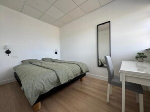 Um quarto com cama, mesas de cabeceira, escrivaninha e espelho.