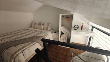 Ein Schlafzimmer mit einem Bett, einem Nachttisch, einem Schreibtisch und einem Fenster.