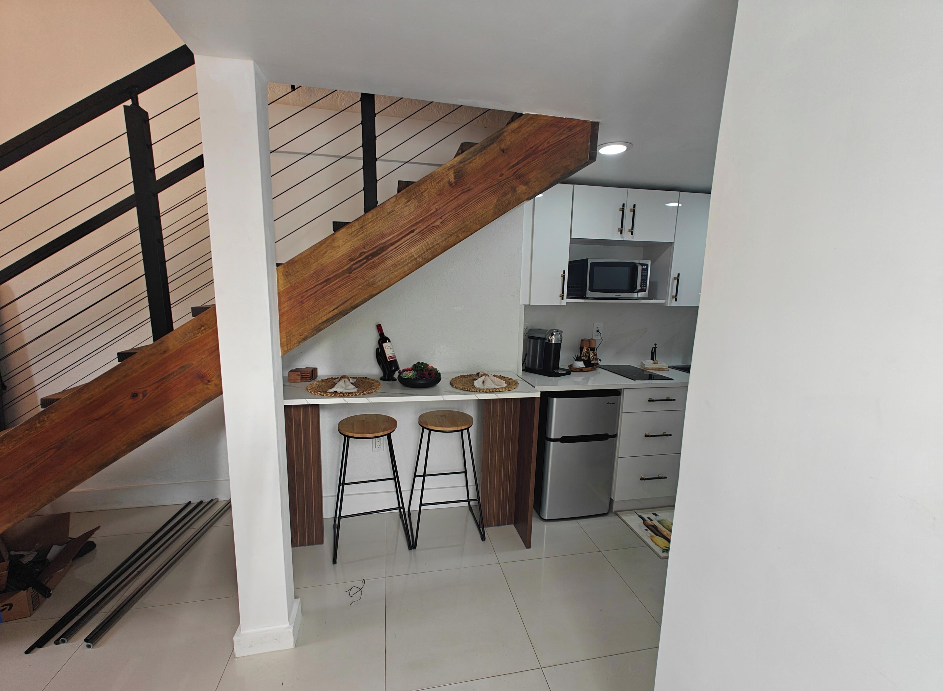 A kitchen with a wooden staircase, white cabinets, a microwave, and a coffee maker.