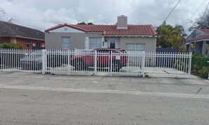 Il s’agit d’une propriété résidentielle dotée d’une allée clôturée, dans laquelle est garé un véhicule rouge, et d’une maison dont le toit est recouvert de tuiles rouges.